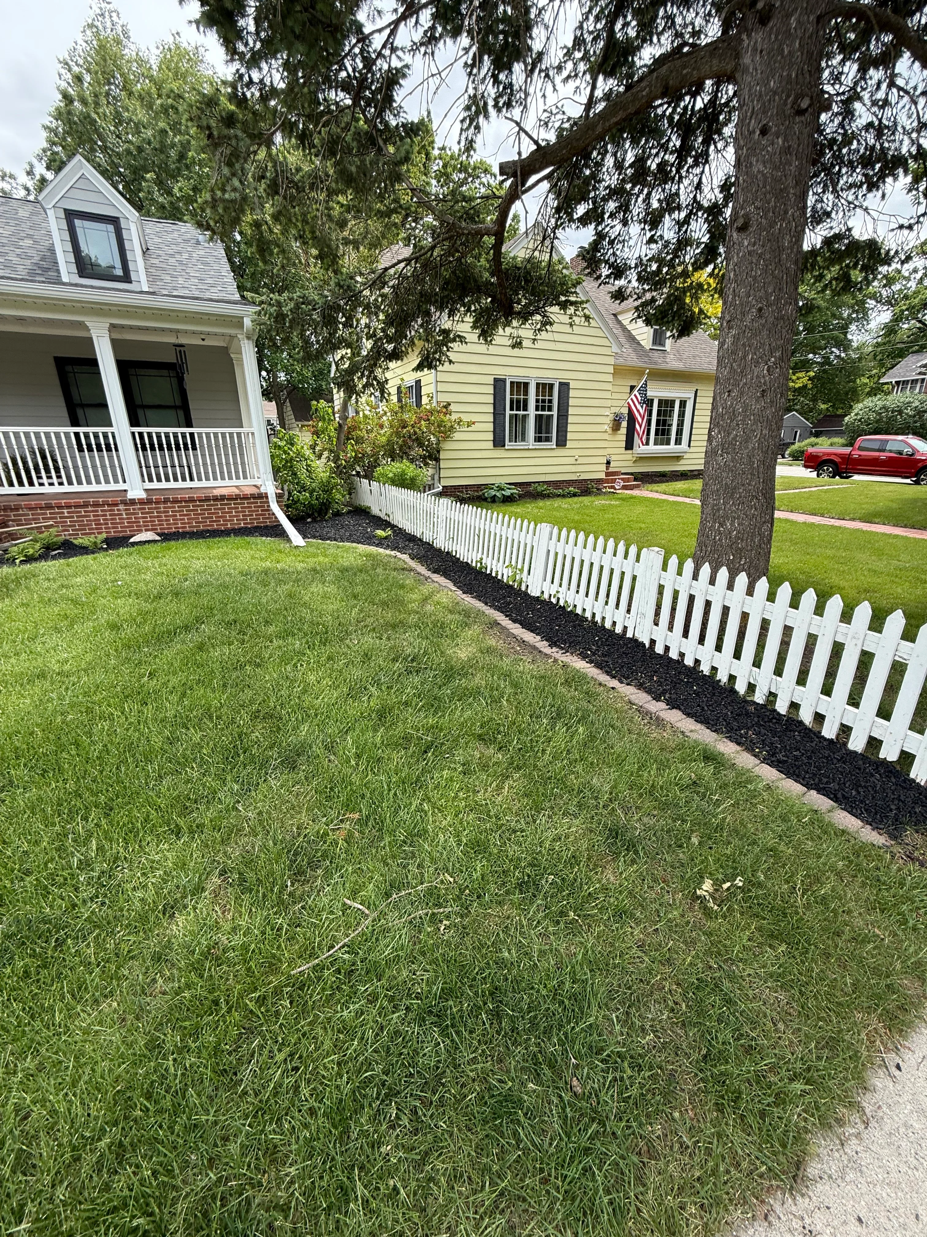 White picket fence with black mulch landscaping bed in front yard