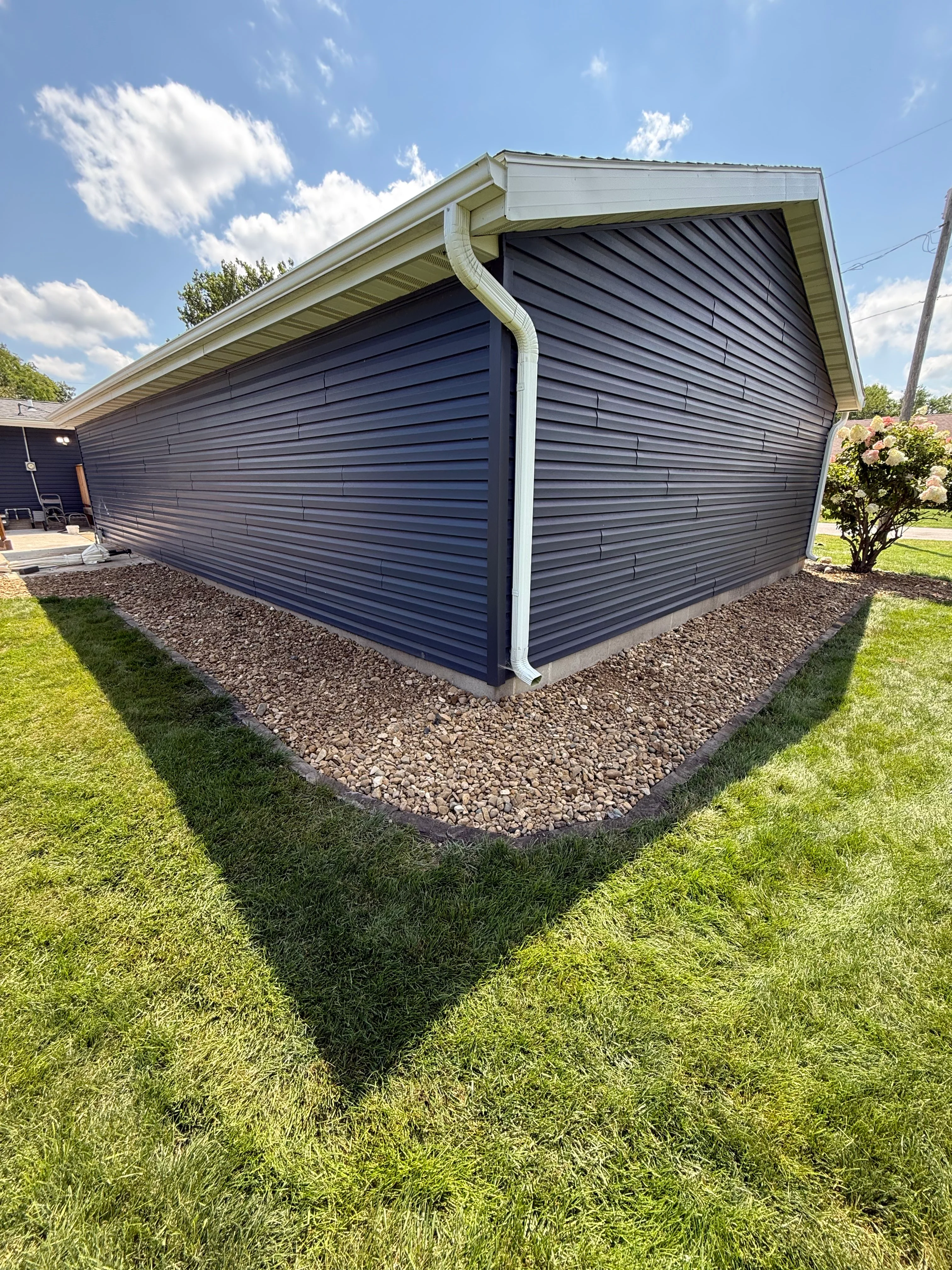 Newly landscaped garage foundation with gravel bed, black metal edging, and manicured lawn