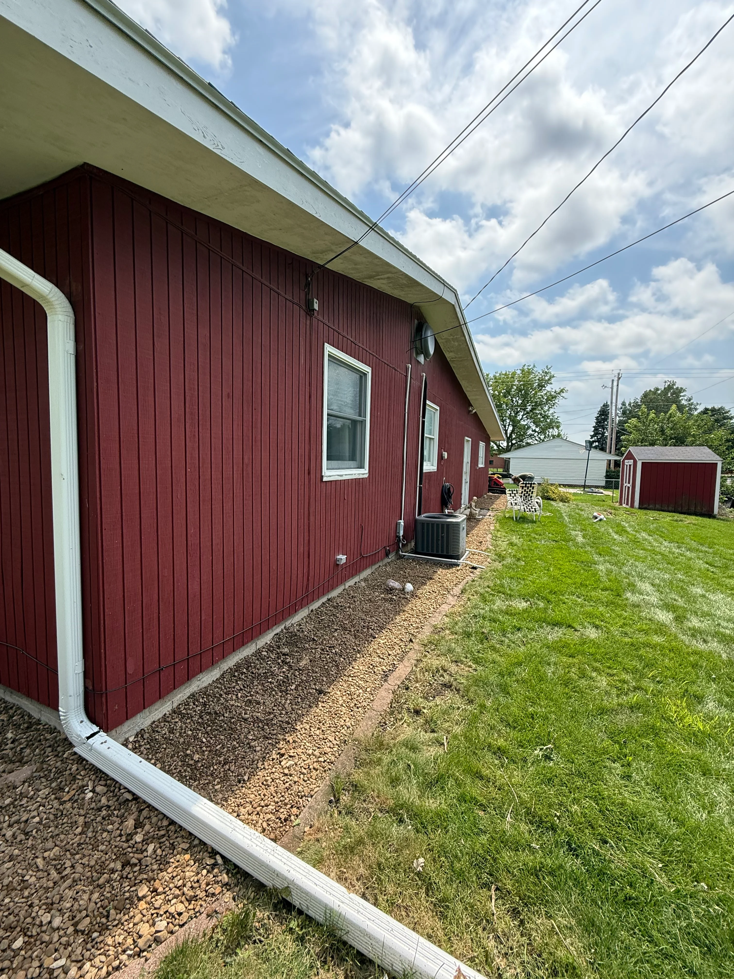 Red metal building with white trim and gravel drainage base installed around foundation