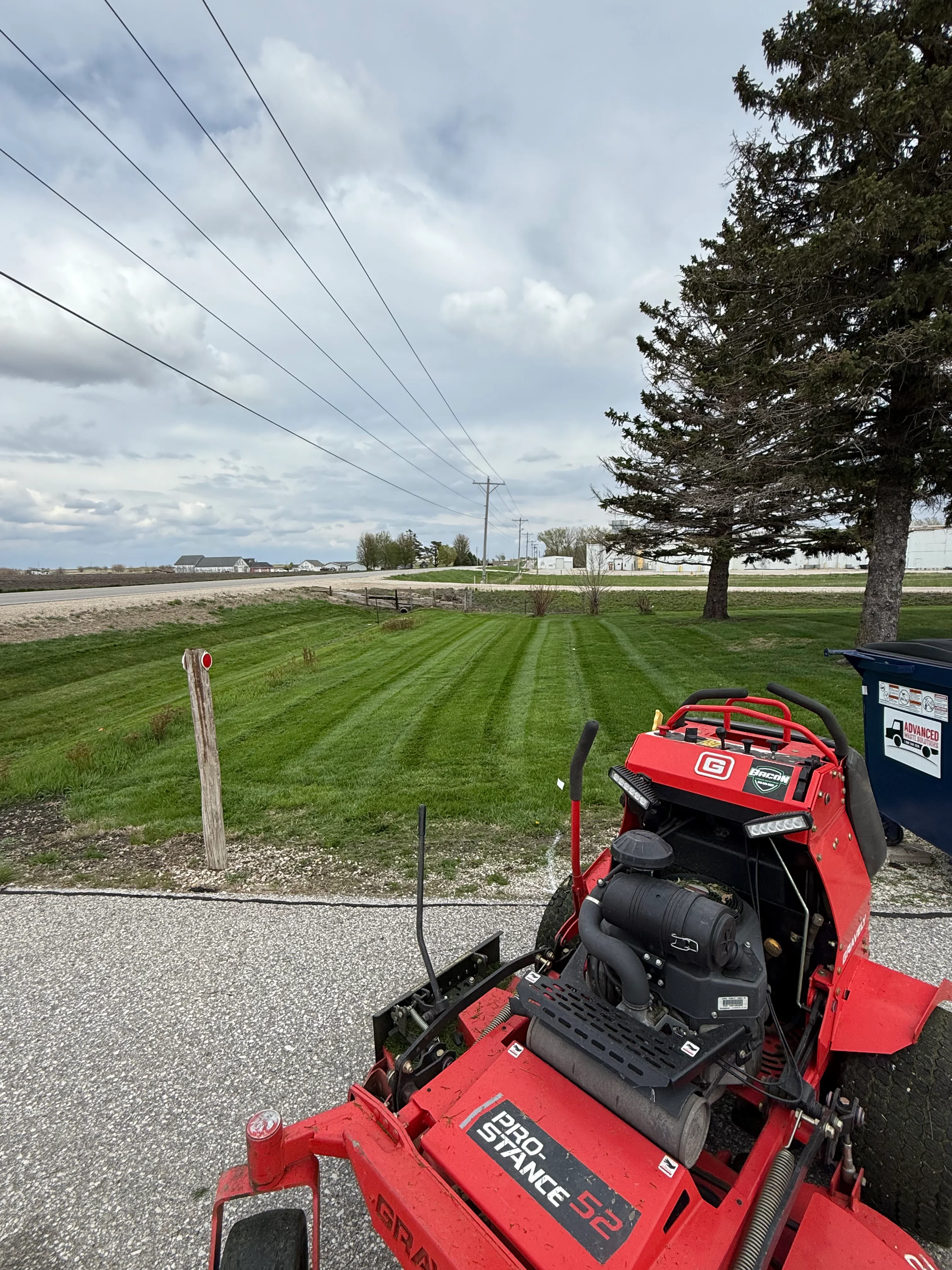 Red zero-turn mower on striped residential lawn with rural property in background