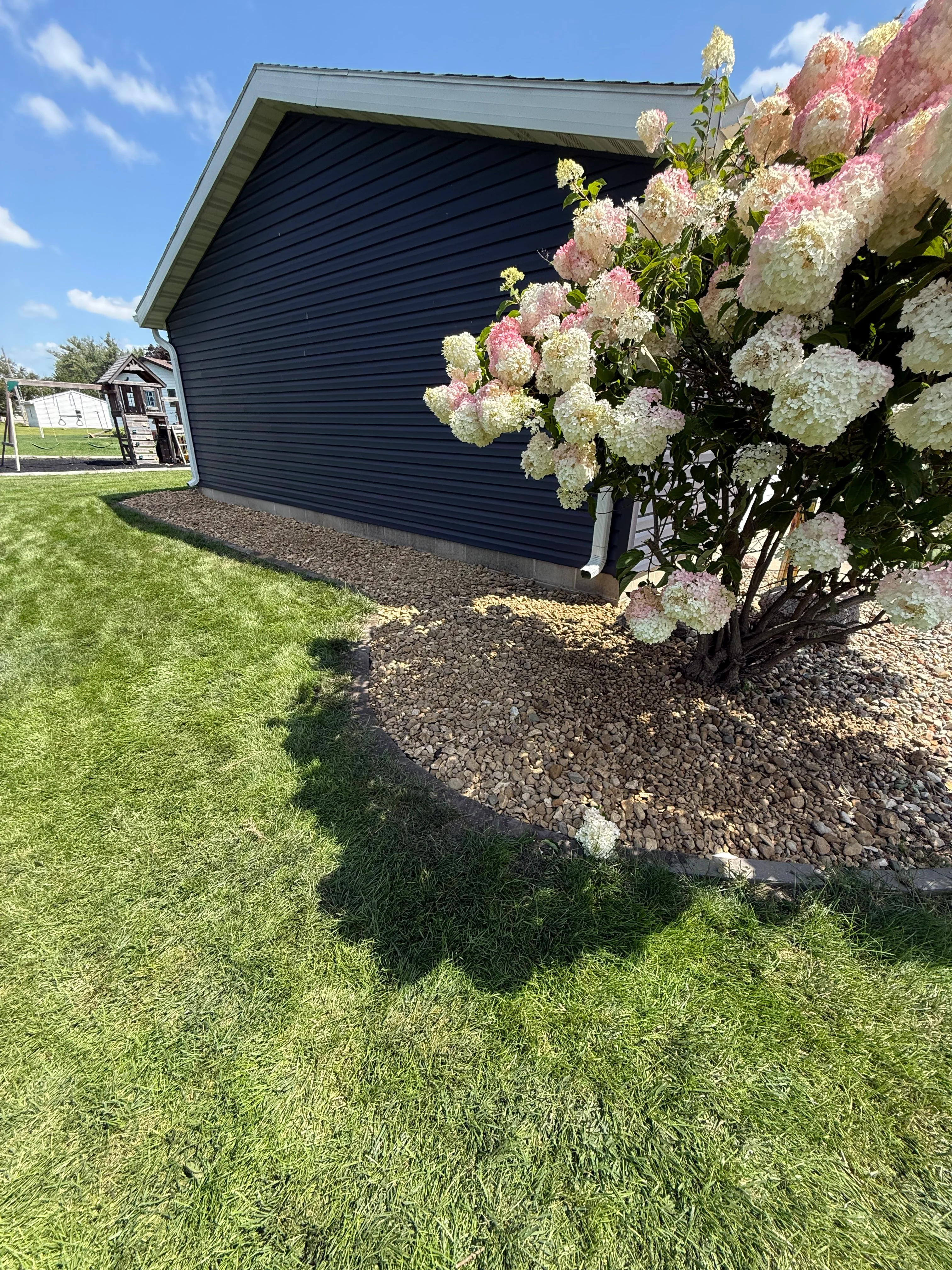 Dark garage with new gravel landscape bed and blooming pink and white hydrangeas