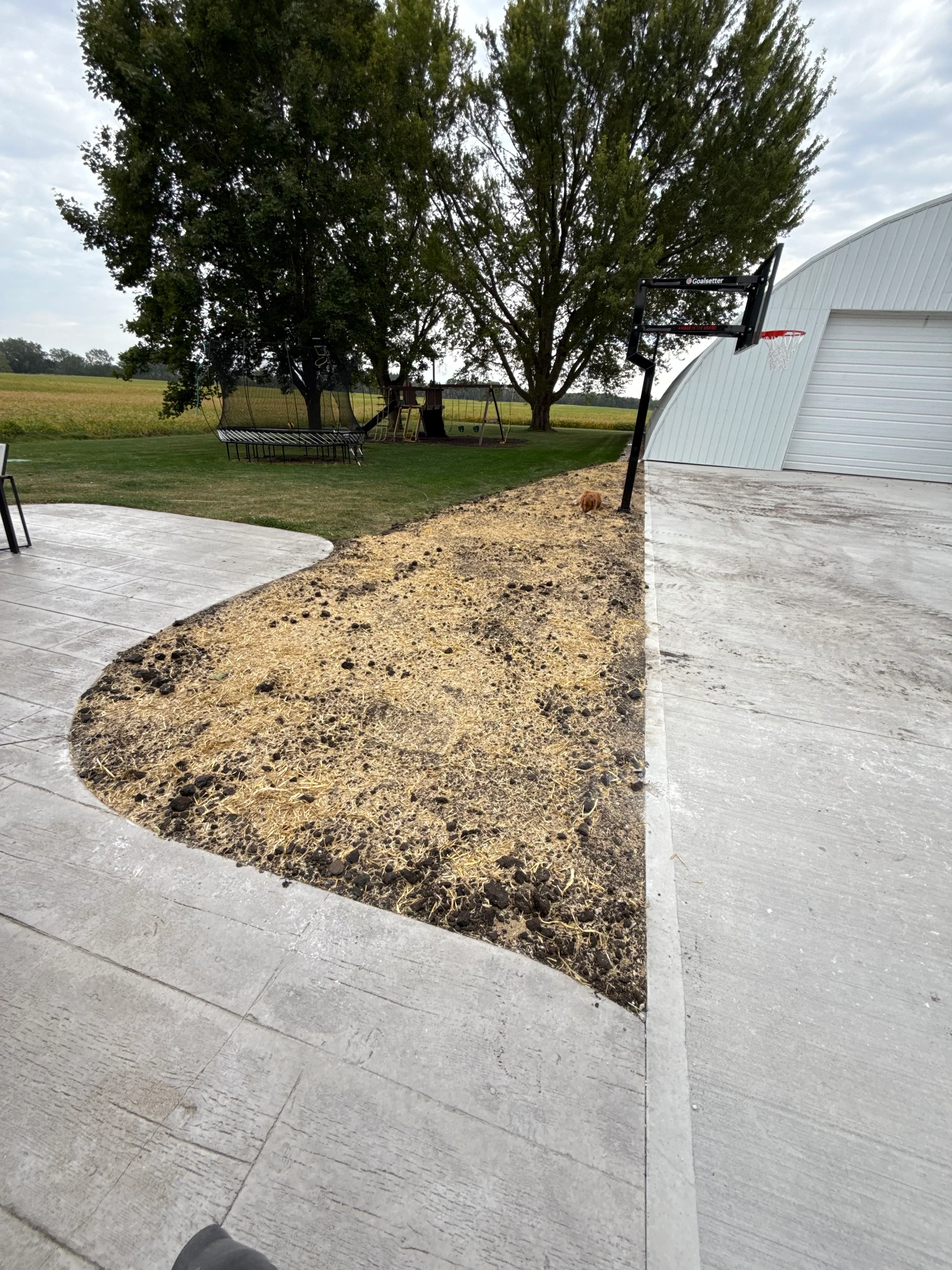Concrete patio with curved gravel bed edging and metal building backdrop