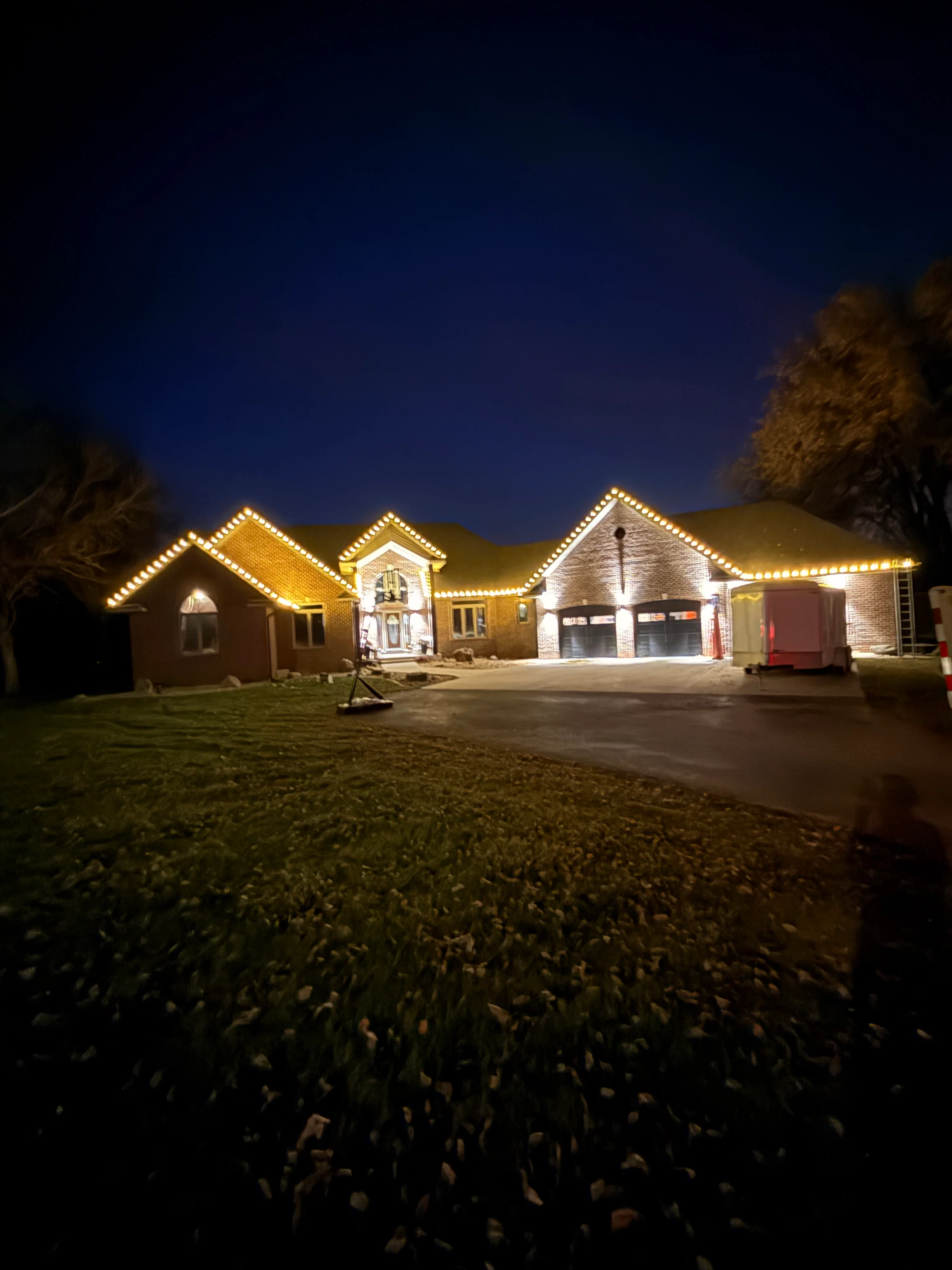 Brick home at night with warm white Christmas lights outlining roofline and architectural features