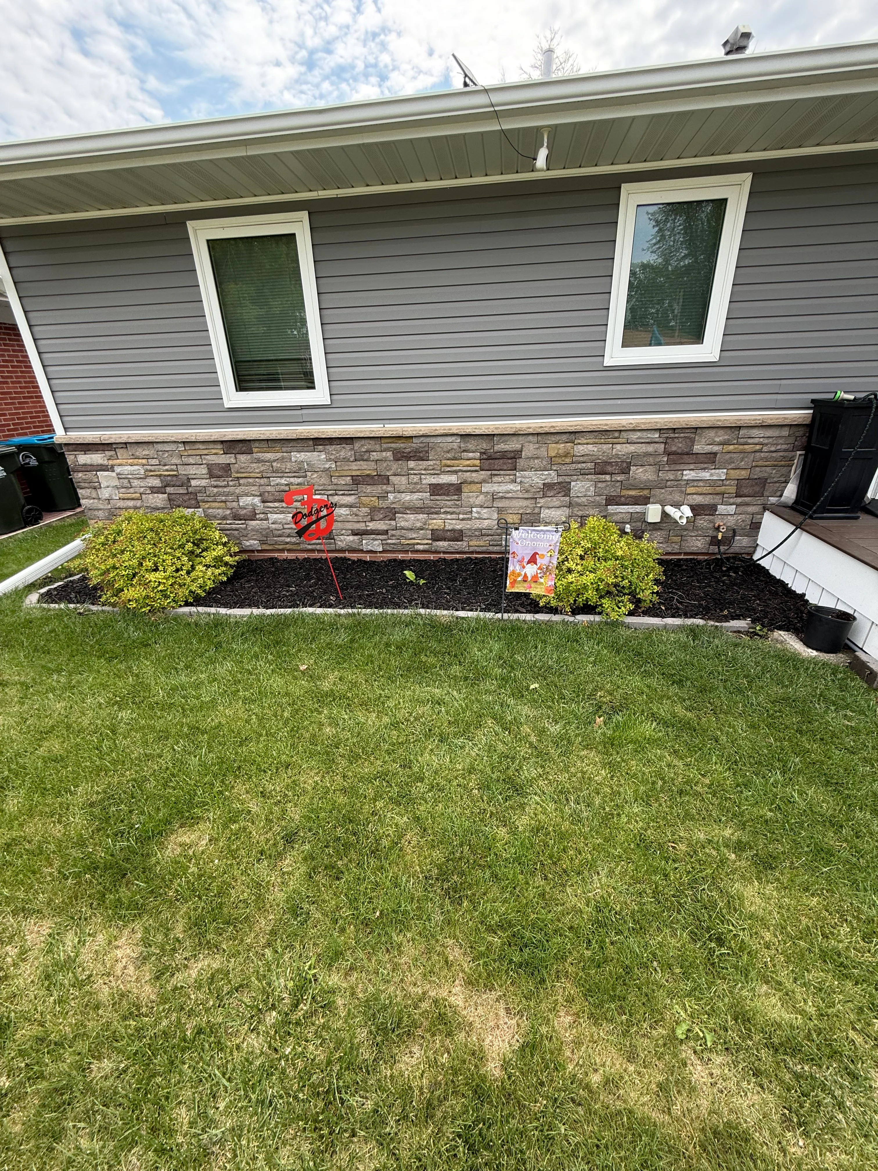 Stone veneer foundation with black mulch beds and yellow-green shrubs