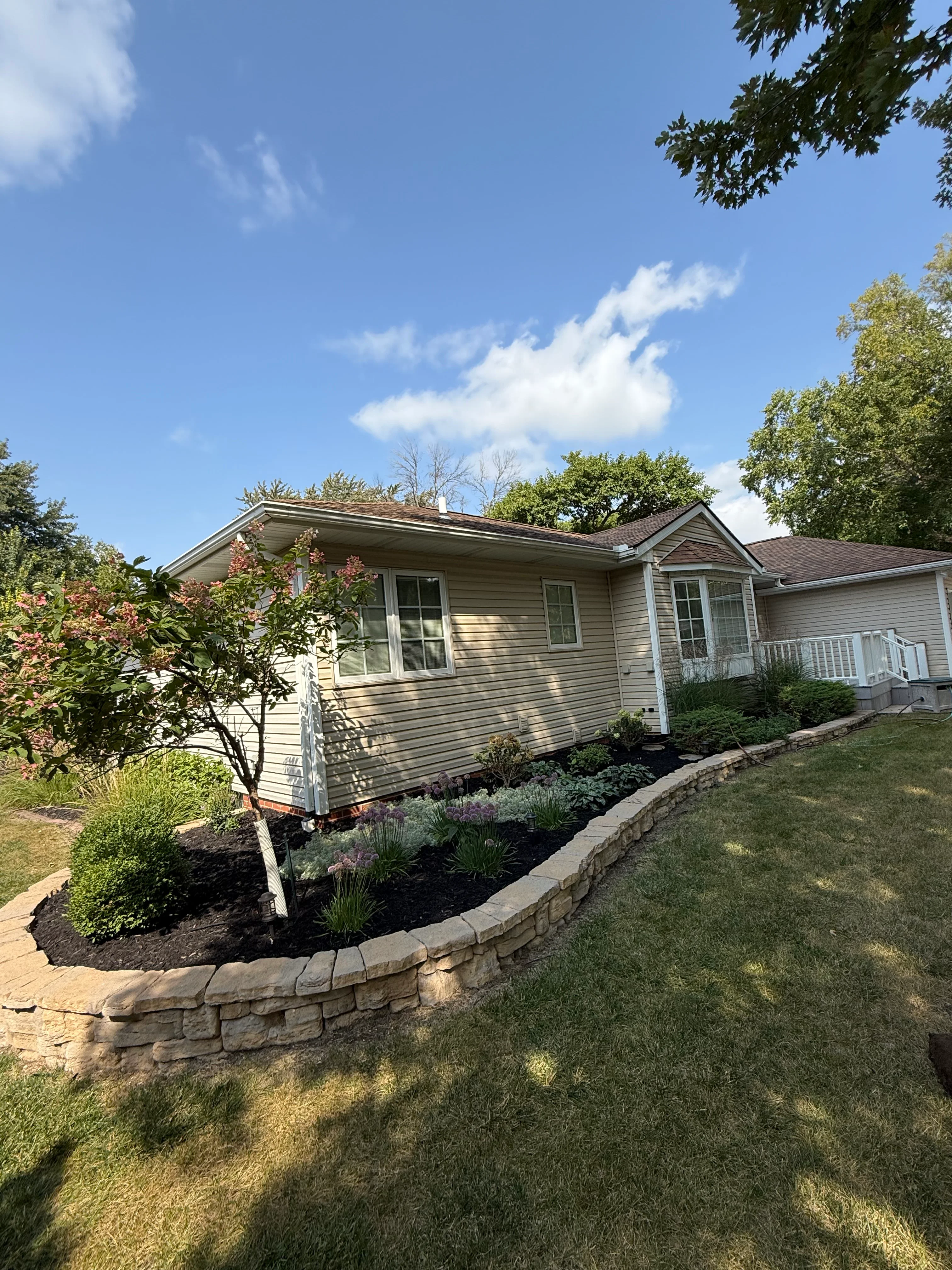 Single-story home with new curved stone retaining wall, mulched landscape beds, and flowering shrubs