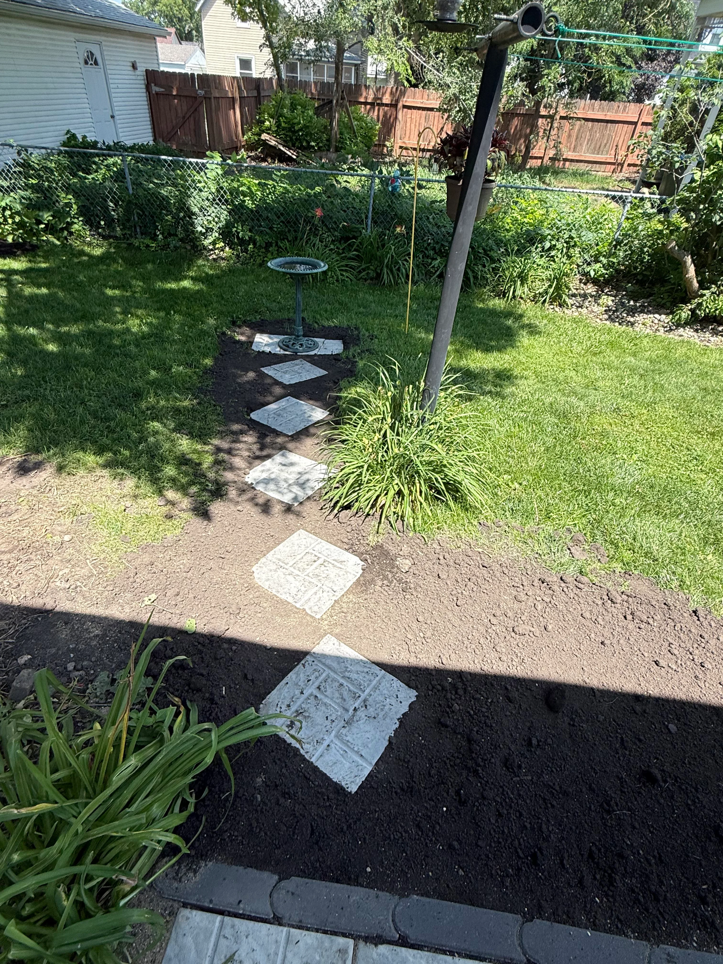 Concrete stepping stone pathway through landscaped backyard with mulch beds and ornamental plants