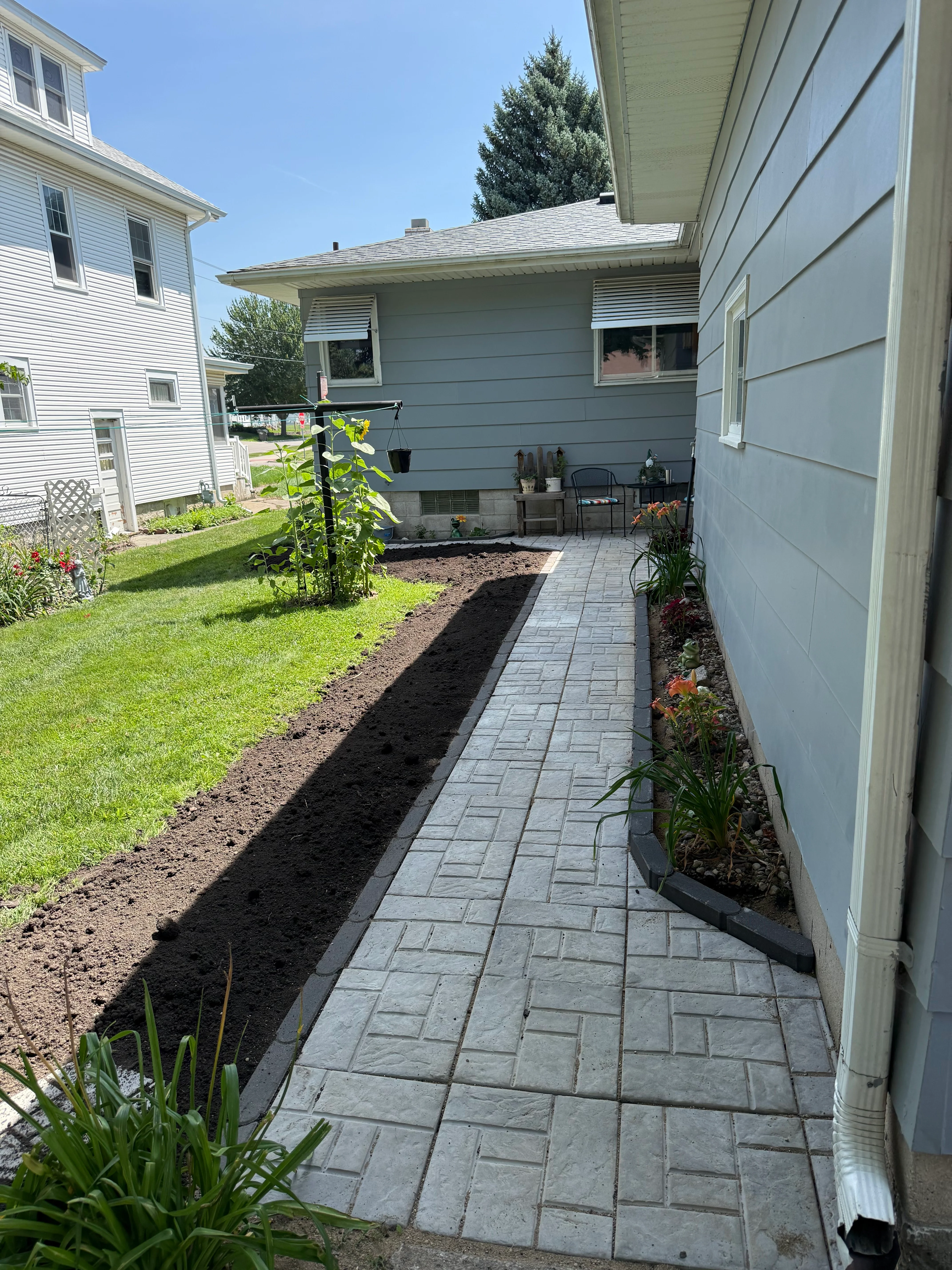 Gray concrete paver walkway with new mulch beds and plantings along home exterior