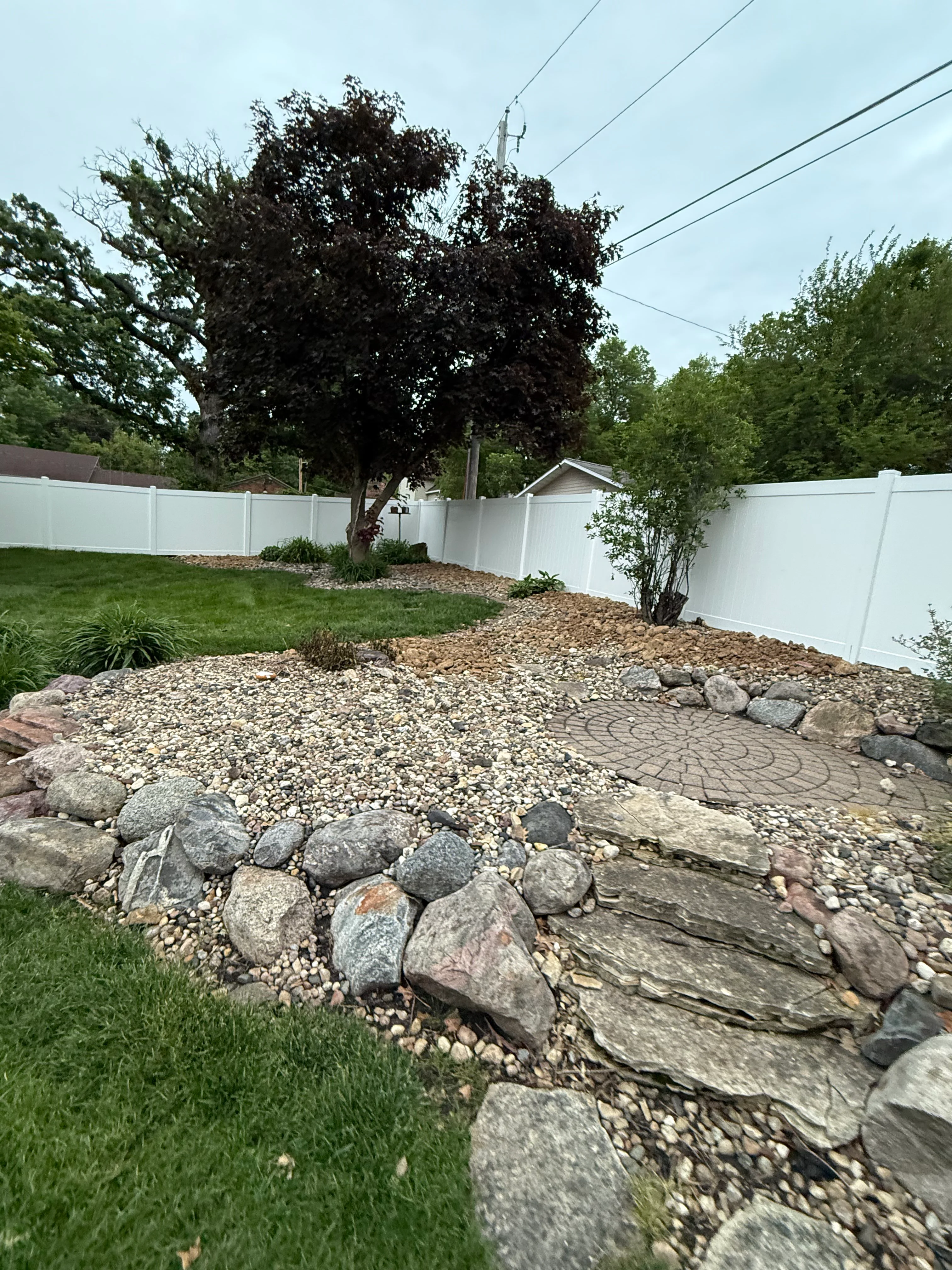Backyard landscape with white vinyl fence, river rock bed, boulders, and paver patio